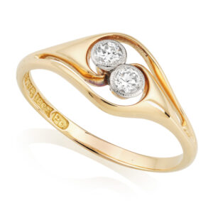 An 18ct yellow gold Art Nouveau two stone diamond crossover ring containing millegrain set old brilliant cut diamonds. Circa 1910.