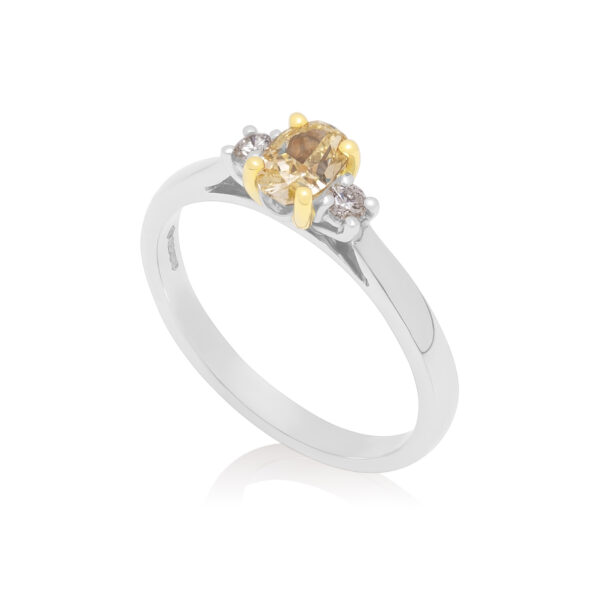 Platinum oval yellow diamond and brilliant cut diamond three stone ring with an 18ct yellow gold claw setting.