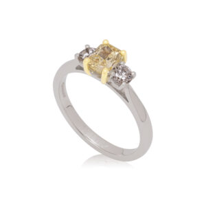 A platinum radient cut yellow diamond and round brilliant cut diamond three stone ring with an 18ct yellow gold claw setting.