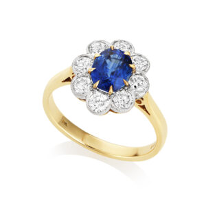 An 18ct yellow and white gold oval sapphire and round brilliant cut diamond cluster ring with millgrain settings, containing nine stones.