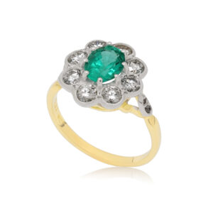 An 18ct yellow and white gold oval shaped emerald and round brilliant cut millegrain set diamonds, with diamonds set to the shoulders.