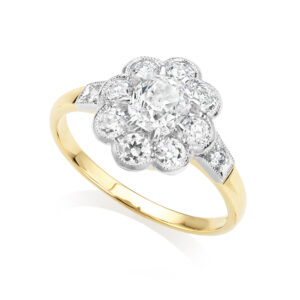 An 18ct yellow gold and platinum mounted Victorian style oval diamond cluster ring. The centre old mine cut diamond is accompanied with millegrain set outer brilliant cut diamonds with further diamonds to each shoulder.
