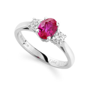 An 18ct white gold oval shaped ruby and brilliant cut diamond three stone ring. Hallmarked Birmingham 2009.