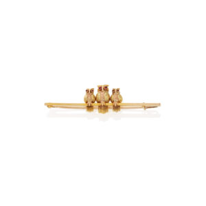 An early 20th century 9ct gold brooch consisting of three multi-coloured gold and textured owls, each with cabochon ruby eyes, perched on a plain gold bar.