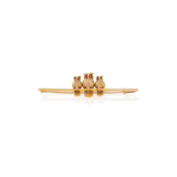 An early 20th century 9ct gold brooch consisting of three multi-coloured gold and textured owls, each with cabochon ruby eyes, perched on a plain gold bar.