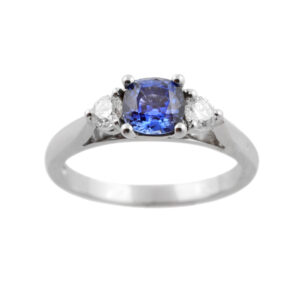 A platinum cushion shaped sapphire and brilliant cut diamond three stone ring.