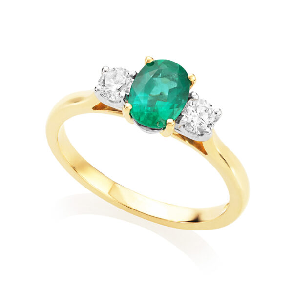 An 18ct yellow and white gold oval emerald and diamond three stone ring. The oval emerald sits between two round brilliant cut diamonds.