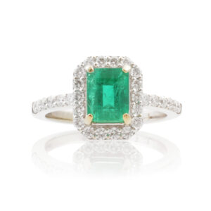 An 18ct white and yellow gold emerald and brilliant cut diamond cluster ring with diamond set shoulders.