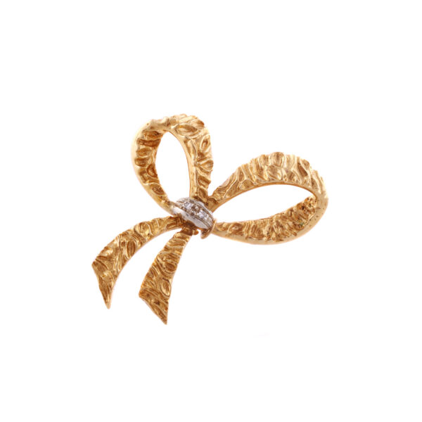 An 18ct yellow gold diamond set bow brooch, with a hammered effect on the ribbon with diamonds on the centre knot.