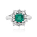 A platinum emerald cut emerald cluster ring surrounded by ten round brilliant cut diamonds.