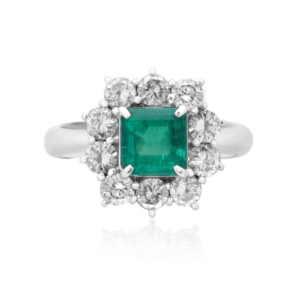 A platinum emerald cut emerald cluster ring surrounded by ten round brilliant cut diamonds.