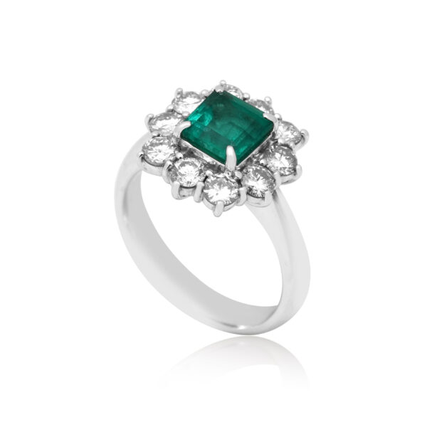A platinum emerald cut emerald cluster ring surrounded by ten round brilliant cut diamonds.