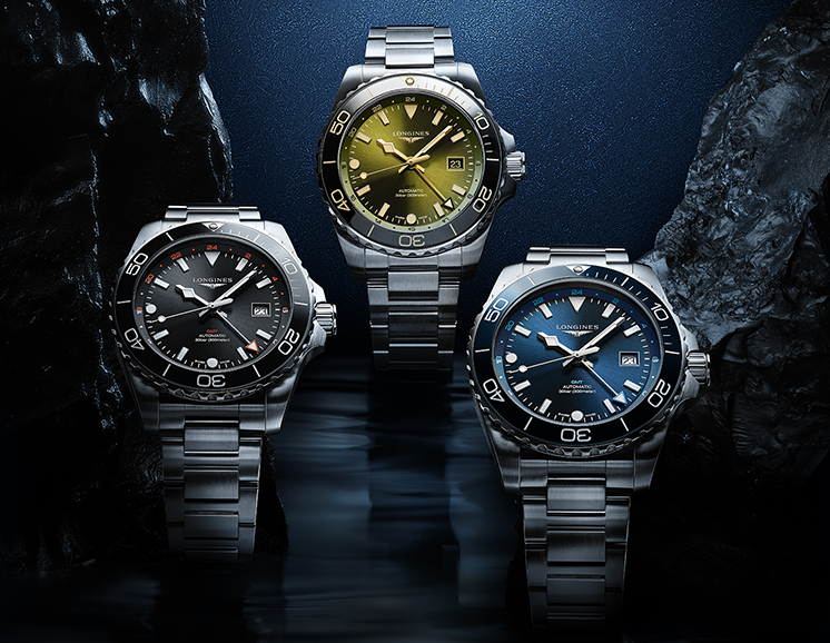 Three Longines Conquest watches on a dark blue background appearing as though they are under water.
