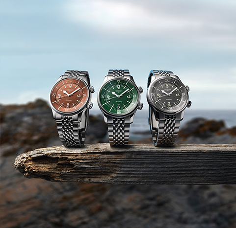Three Longines watches placed on a rock with orange, green and grey dials.