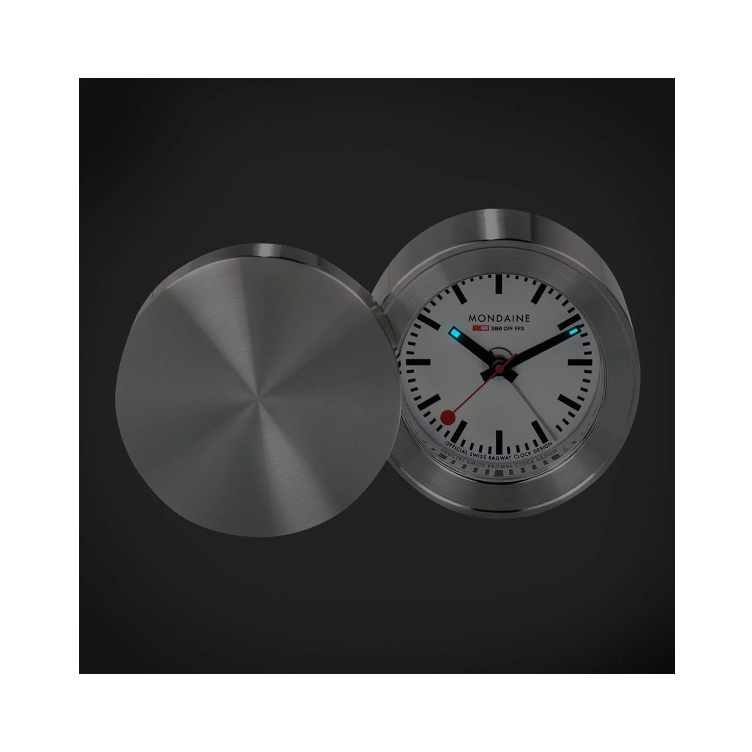 Mondaine, Travel Alarm Clock Mondaine, Travel Alarm Clock with a 50mm brass stainless steel pressed case with an alarm function and a white dial.