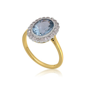 An Edwardian 18ct yellow gold and platinum aquamarine and diamond oval cluster ring. The millegrain set oval faceted aquamarine is surrounded by twenty two similarly set old eight cut diamonds.