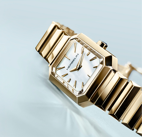 A yellow gold tone Herbelin Octogone women's watch on a light blue background.