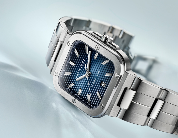 A stainless steel, blue dial Herbelin Cap Camarat watch on a light blue background.