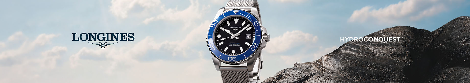 A Longines HydroConquest stainless steel case and bracelet watch on a blue sky background with a mountain peak in view.
