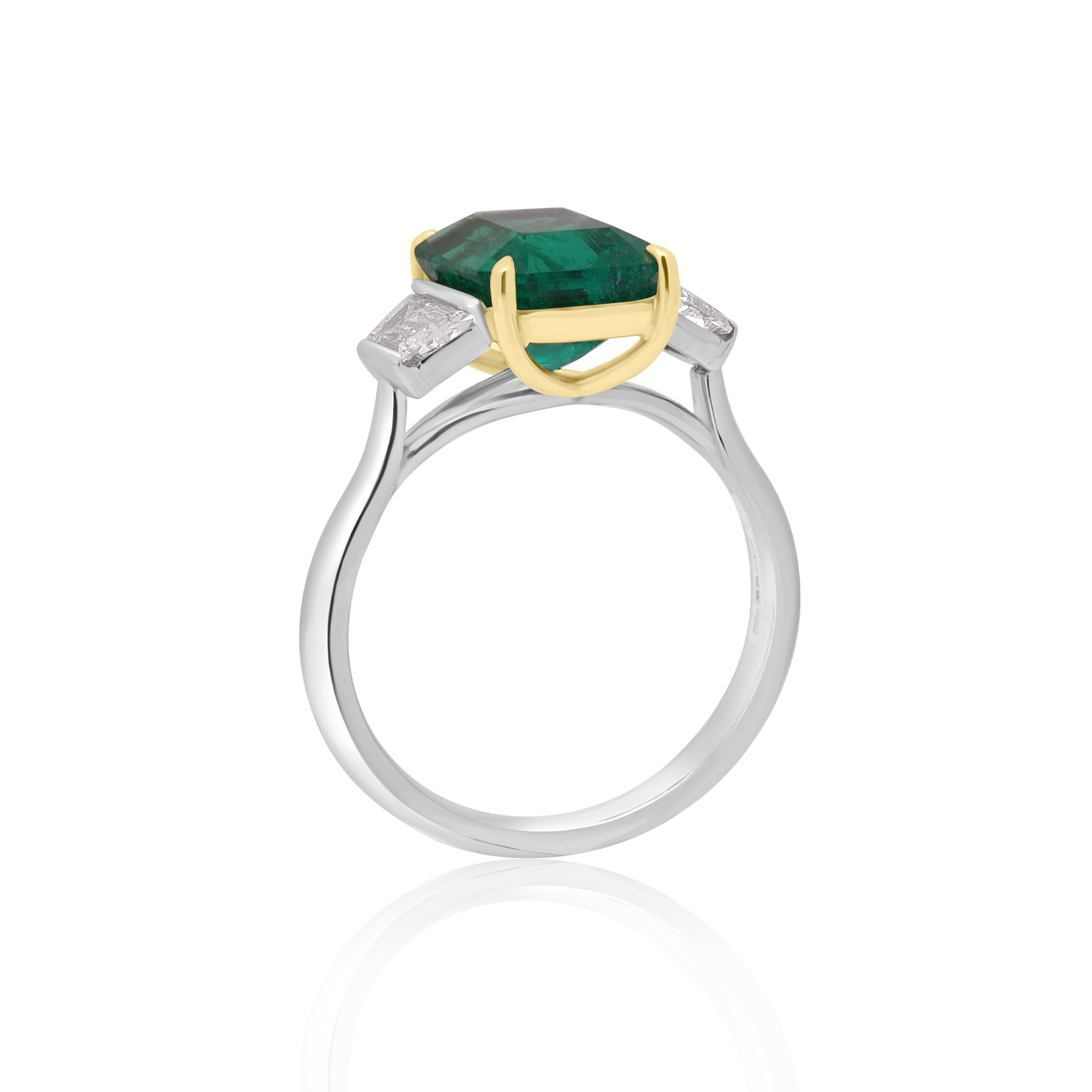A platinum green emerald and trapeze cut diamond three stone ring.