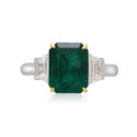 A platinum green emerald and trapeze cut diamond three stone ring.
