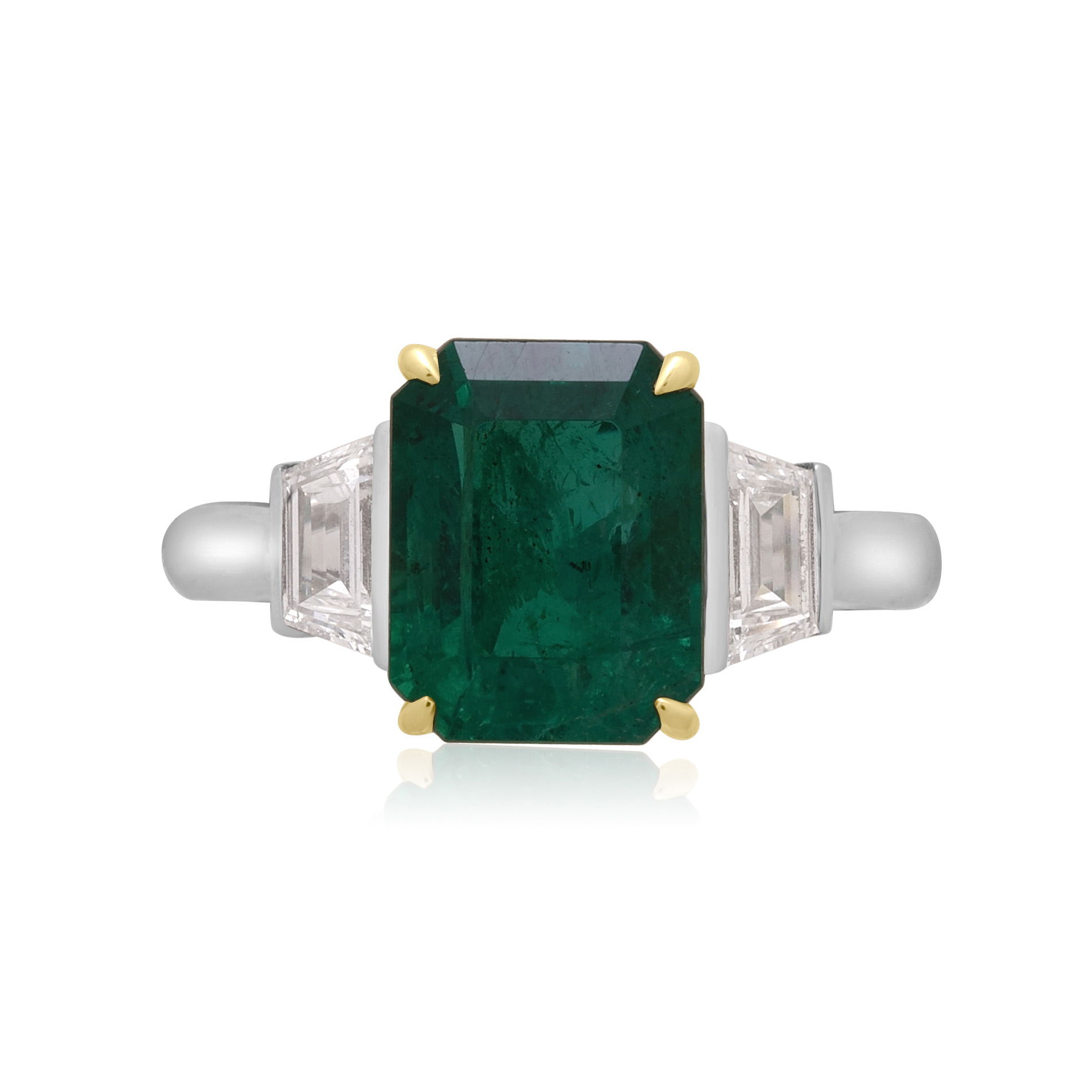 A platinum green emerald and trapeze cut diamond three stone ring.
