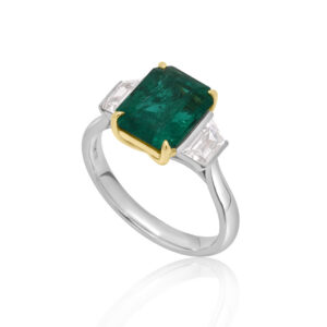 A platinum green emerald and trapeze cut diamond three stone ring.