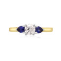 An 18ct yellow and white gold pear shaped sapphire and round brilliant cut diamond three stone ring.