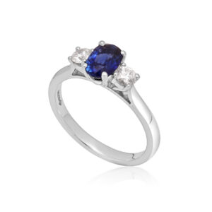A platinum oval sapphire and round brilliant cut diamond three stone ring.
