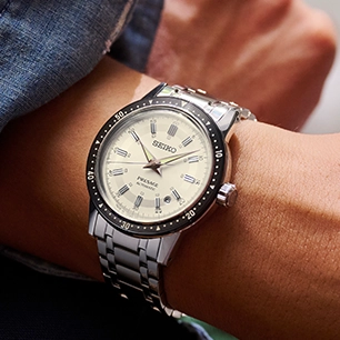 A stainless steel Seiko with a white dial and black bezel on a man's wrist.
