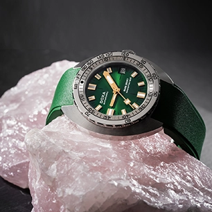 A DOXA watch with a green dial and green strap laying on a pink rock.