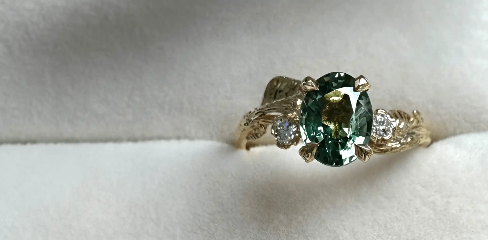 A yellow gold bespoke ring with a green gemstone sitting in a cream coloured ring holder.