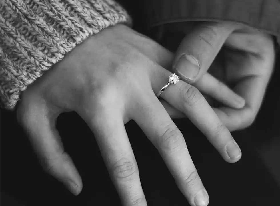 A couple holding hands with the woman's hand wearing a diamond engagement ring.