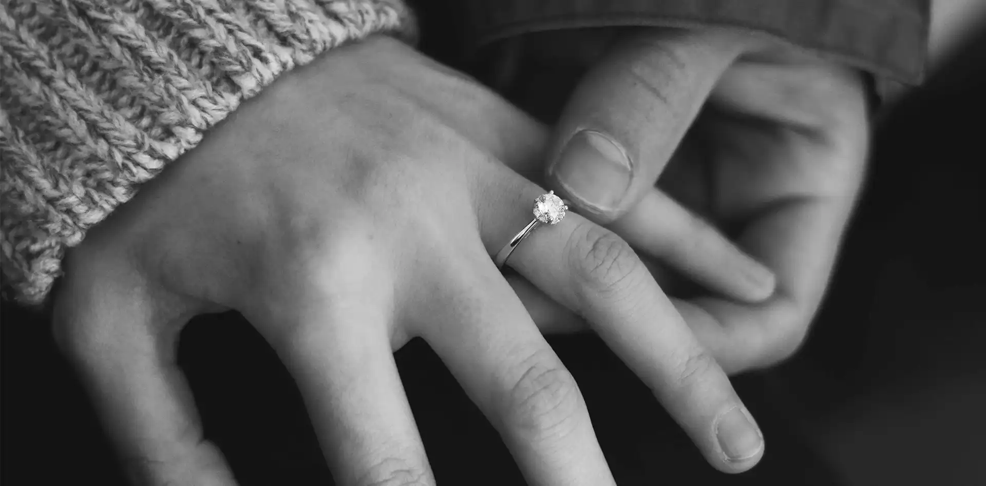 A couple holding hands with the woman's hand wearing a diamond engagement ring.
