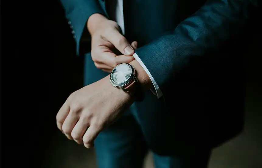 A man wearing a dark blue suit wearing a watch on his wrist.