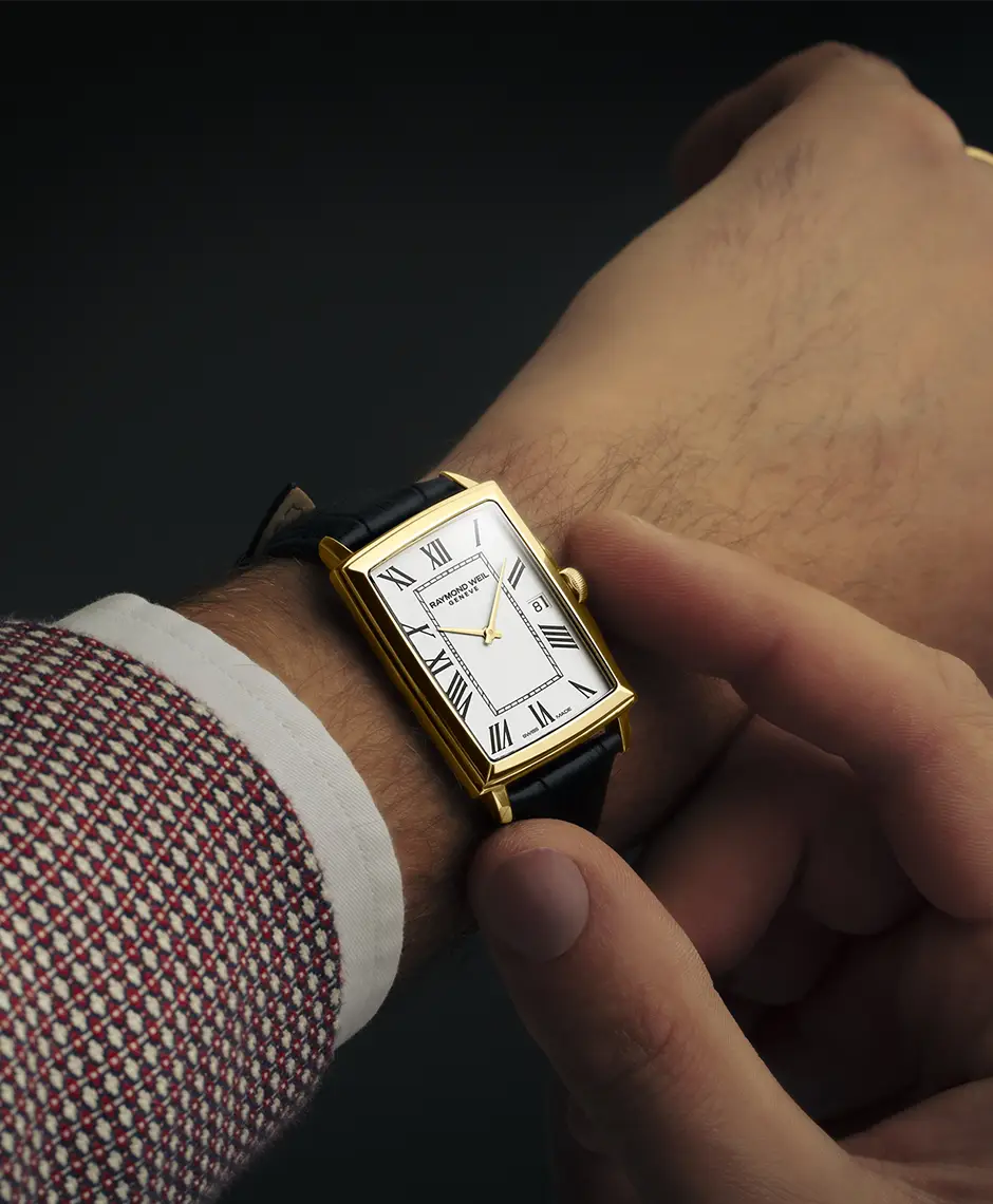 A Raymond Weil Toccata watch with a rectangular case and a leather strap on a man's wrist wearing a suit.