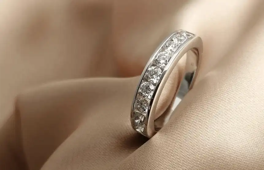 A white gold diamond set eternity ring on a champagne coloured cloth background.