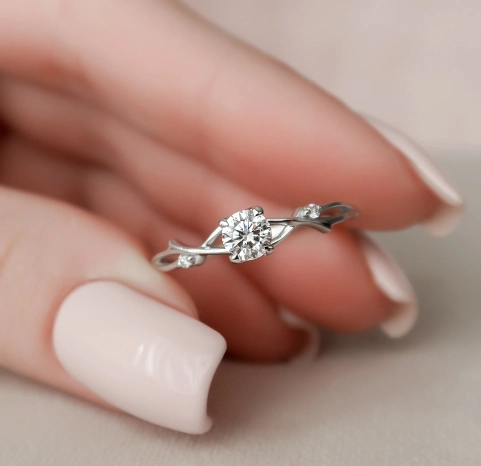 A woman's hand with light pink pastel painted nails holding a white gold diamond single stone ring.