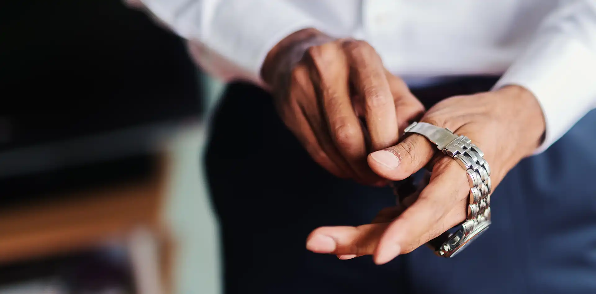 A man wearing a suit putting a watch on his wrist.