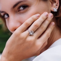 A woman holding her hand up to her face, wearing a diamond solitaire ring.