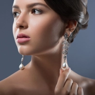 A woman with dark brown hair, looking over her shoulder, wearing pearl drop earrings.